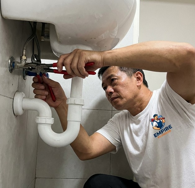 Empire Plumber technician using wrench to repair pipes under sink